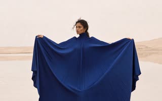 A model in a blue cape standing in shallow water in the desert