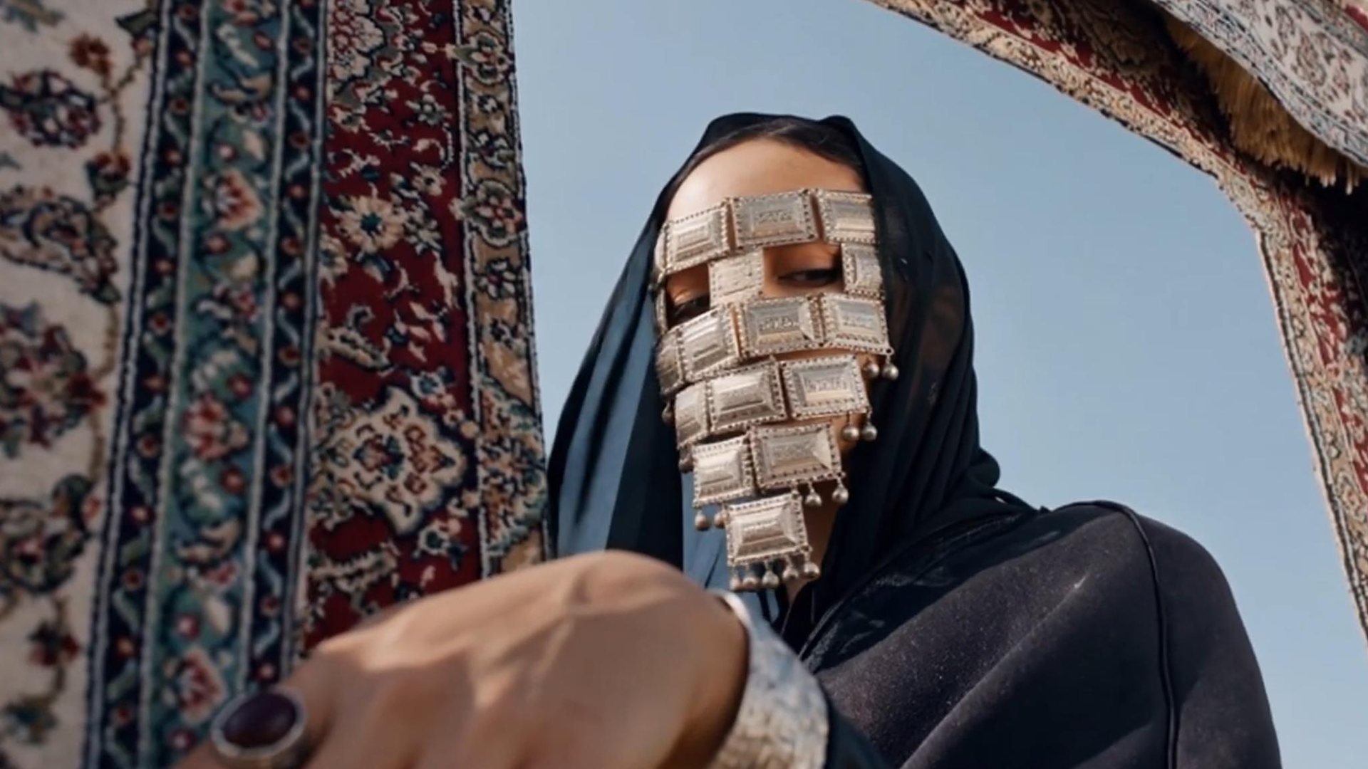 A woman in a silver face veil between hanging carpets, a frame from dotMD's Saudi National Day film